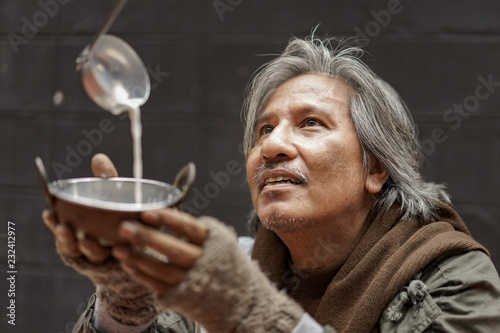 Tableau sur toile Older homeless dirty poor beggar man look at donor and using metal bowl to receive some milk from them and waiting to help from them