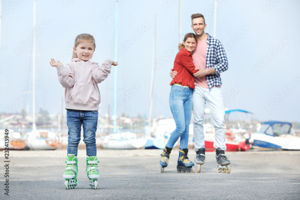 Fototapeta premium Little girl and her parents roller skating on embankment