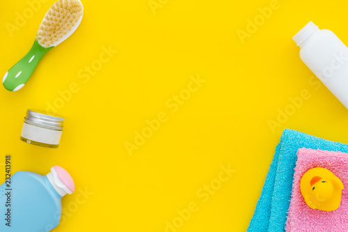 Baby care. Bath cosmetics and accessories for child. Shampoo  gel  cream  comb  yellow rubber duck on yellow background top view copy space