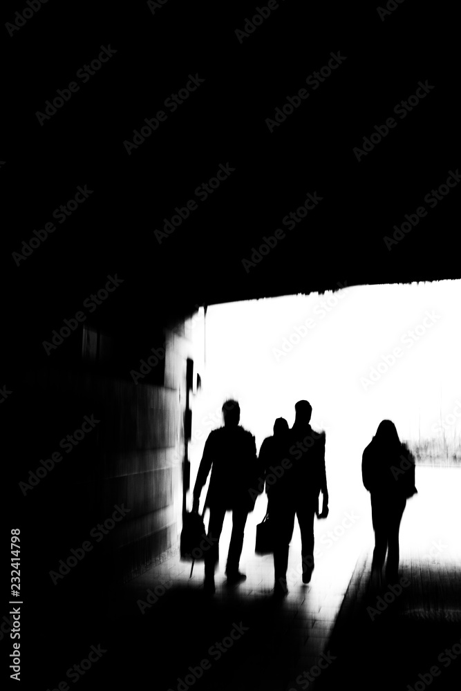Dark silhouette image of four young people walking through a tunnel