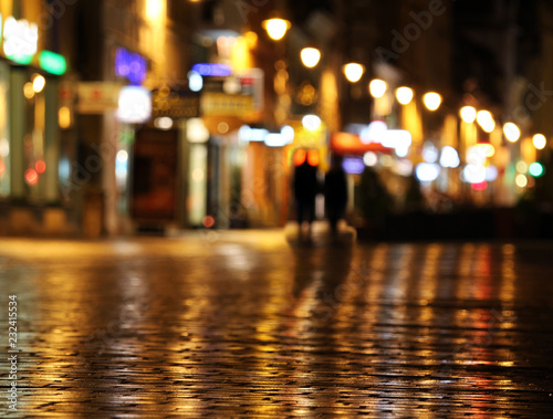 Colorful city lights and shadow of couple walking mirrored in the wet street