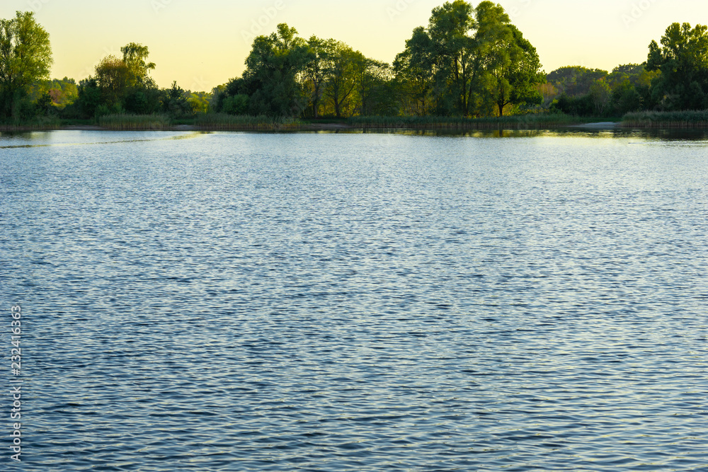 Fototapeta premium Blue lake with cloudy sky, nature series, a lake landscape with reflection from some trees.