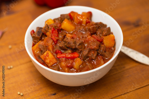 Meat stew with beef, potato, carrot, onion, spices,tomato and pepper . Slow cooked meat stew, bowl, wooden background. Hot autumn-winter dish. Close up.