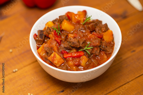 Meat stew with beef, potato, carrot, onion, spices,tomato and pepper . Slow cooked meat stew, bowl, wooden background. Hot autumn-winter dish. Close up.