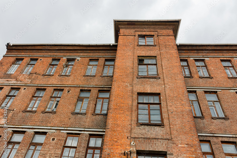 Upward view to old red brick wall building with windows and cloudy sky on the background Upward view to old red brick wall building with windows and cloudy sky on the background