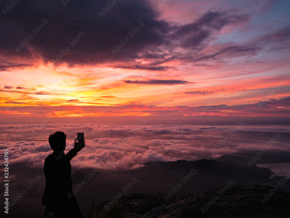 Silhouette People Take a Selfie on the cliff with beautiful sunrise sky on Khao Luang mountain in Ramkhamhaeng National Park,Sukhothai province Thailand