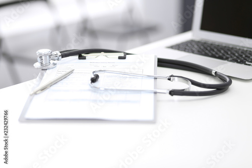 Stethoscope  clipboard with medical form lying on hospital reception desk with laptop computer. Medical tools at doctor working table.Medicine a     health care concept