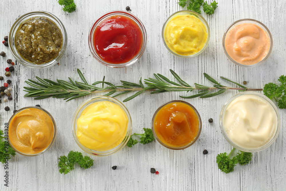 Different tasty sauces in bowls with spices on white wooden table Different tasty sauces in bowls with spices on white wooden table