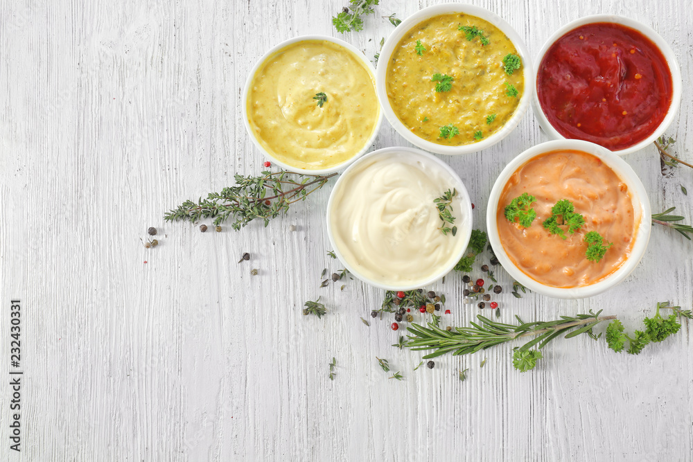 Different tasty sauces in bowls with spices on white wooden table Different tasty sauces in bowls with spices on white wooden table