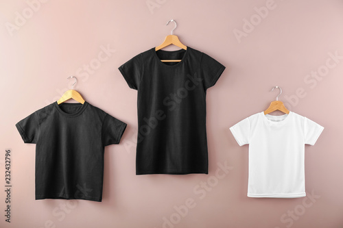 Hangers with blank t-shirts on color background photo