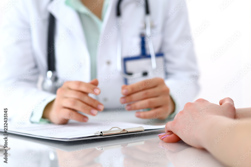 Doctor and patient talking while sitting at the desk in hospital office, close-up of human hands. Medicine and health care concept Doctor and patient talking while sitting at the desk in hospital office, close-up of human hands. Medicine and health care concept