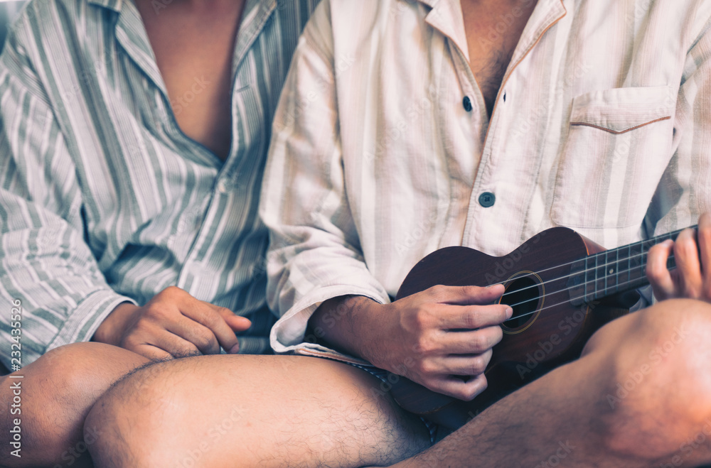Fototapeta premium Young gay couple sitting on sofa and playing guitar