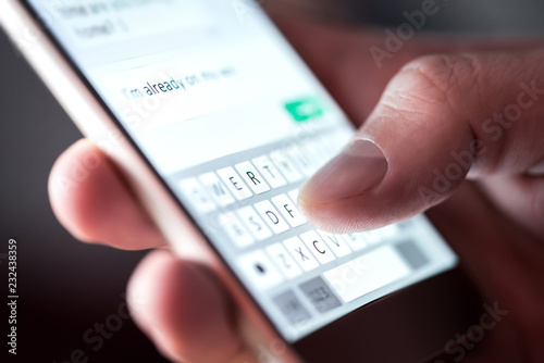 Man sending text message and sms with smartphone. Guy texting and using mobile phone late at night in dark. Communication or sexting concept. Finger typing with cellphone keyboard. Light from screen. photo