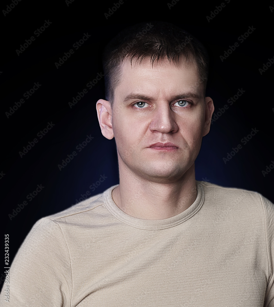 Obraz premium Portrait of a young manly serious man with a short haircut on a black background in a light shirt