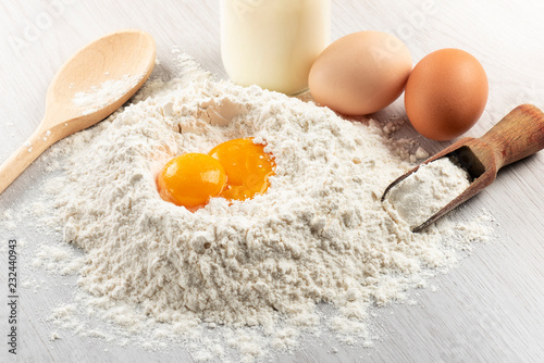 pile of flour with egg yolks and milk bottle on table