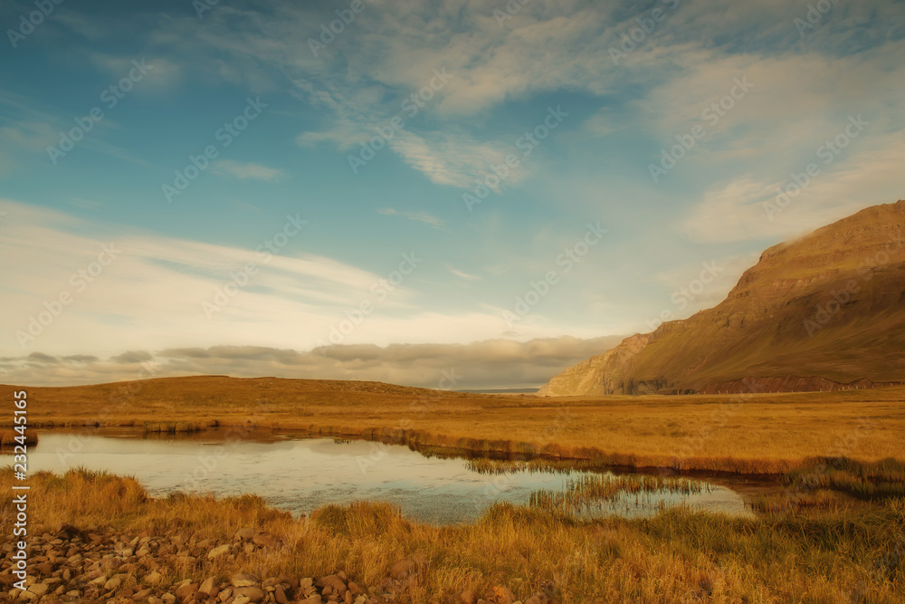 Icelandic landscape. The expanses of fields, a small lake on the background of mountains.
