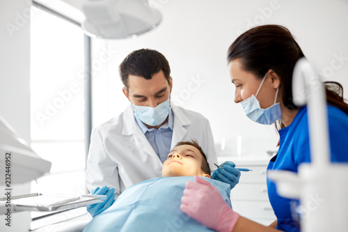 medicine, dentistry and healthcare concept - dentist with mouth mirror and probe checking for kid patient teeth at dental clinic