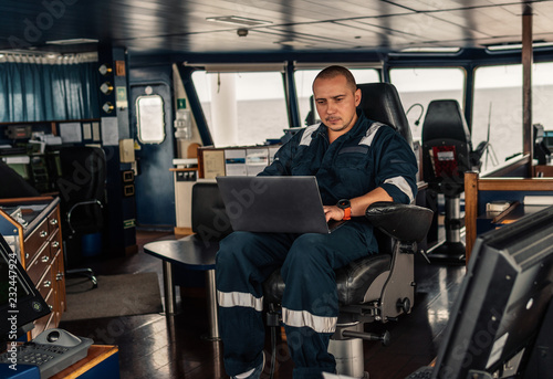 Marine navigational officer or technician is using laptop or notebook at sea. Job at sea