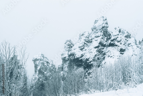 beautiful snow-covered rock over the winter forest during a snowfall