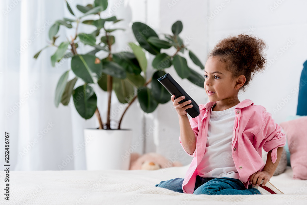 Adorable African american child sitting on the bed and and switching channels on tv Adorable African american child sitting on the bed and and switching channels on tv