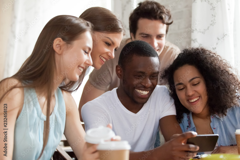 Black guy holding mobile phone watching funny videos with mixed race friends having fun together. Laughing students taking selfie photo looking at cellular screen. Friendship, technology usage concept Black guy holding mobile phone watching funny videos with mixed race friends having fun together. Laughing students taking selfie photo looking at cellular screen. Friendship, technology usage concept