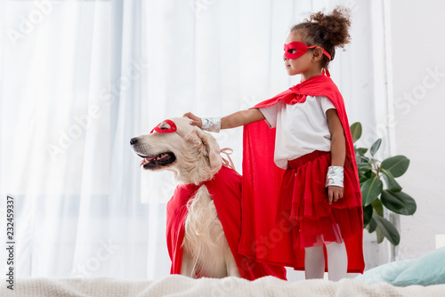 Side view of cute little african american kid and dog standing on the bed photo