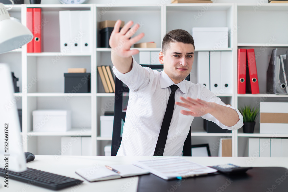 A young man sitting at a computer Desk in the office and spread his hands to the side.