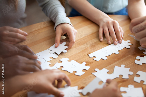 Close up diverse male female hands multiracial people assembling puzzle on wooden table cogitating making decision together. Team building and teamwork, business strategy and logic thinking concept © fizkes