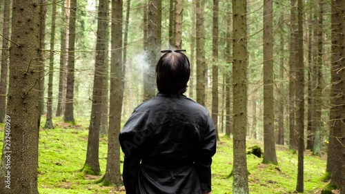 woman standing and smoking in the beautiful green forest, shot from back