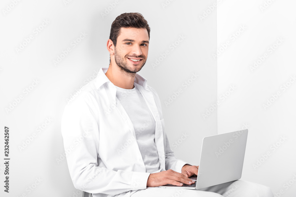 adult smiling handsome man in total white using laptop