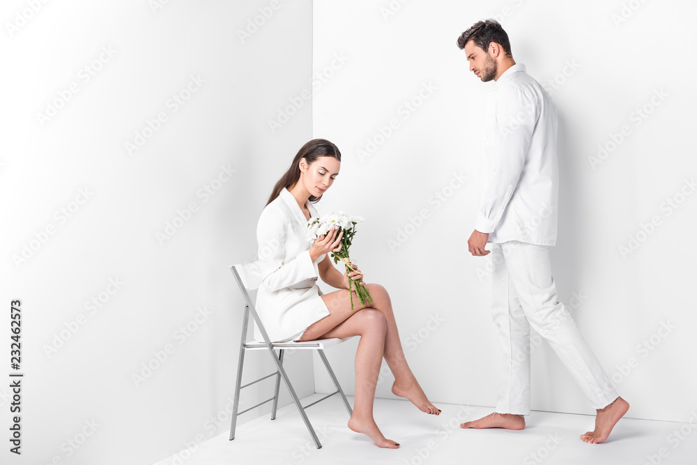 Fototapeta premium adult woman sitting on chair with bouquet while man posing in total white
