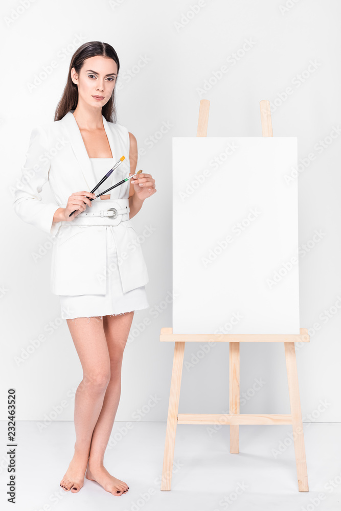 barefoot woman in total white standing near blank easel barefoot woman in total white standing near blank easel