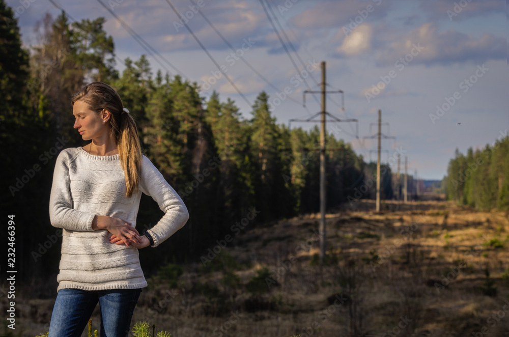 Woman in white knitted sweater posing against the backdrop of a forest clearing in the countryside
