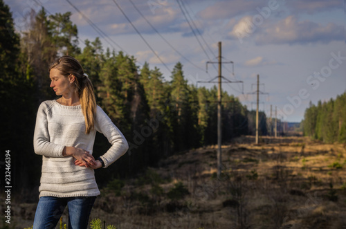 Woman in white knitted sweater posing against the backdrop of a forest clearing in the countryside © Michael Kachalov