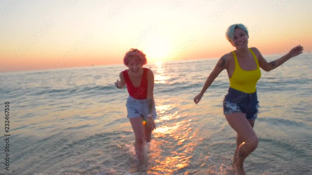 two beautiful women in red and yellow swimsuits having fun on beach during sunset or sunrise two beautiful women in red and yellow swimsuits having fun on beach during sunset or sunrise