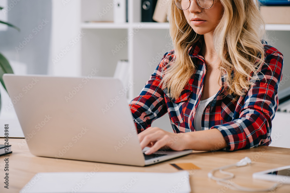 partial view of woman typing on laptop at tabletop with credit card and papers partial view of woman typing on laptop at tabletop with credit card and papers