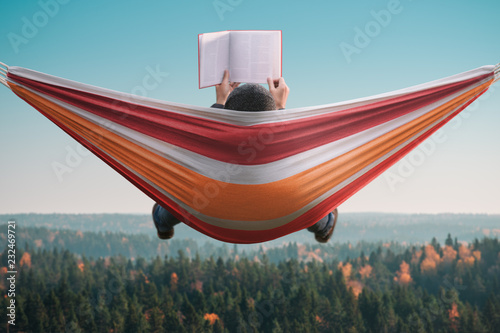 A man sits in a hammock and reads a book in a picturesque place. Back view. photo