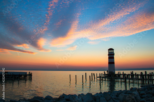 Sunset sky over the sea horizon landscape with lighthouse landmark with wooden dock pillars standing in the water  twilight scenic view from pier of Podersdorf am See  Neusiedl lake in Austria