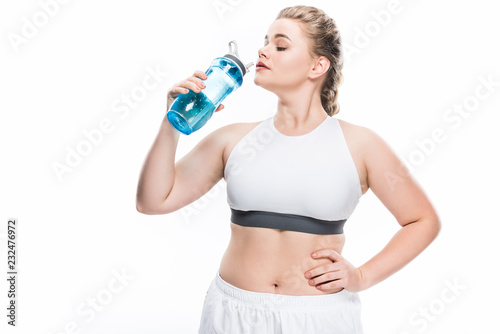 young overweight woman in sportswear drinking water isolated on white