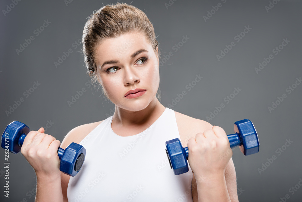 young woman training with dumbbells and looking away isolated on grey young woman training with dumbbells and looking away isolated on grey