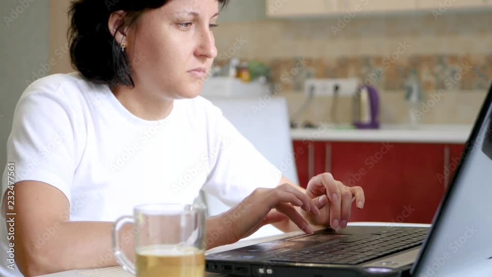 The blogger girl is sitting at the table and using a laptop, there is a cup of tea on the table. The blogger girl is sitting at the table and using a laptop, there is a cup of tea on the table.