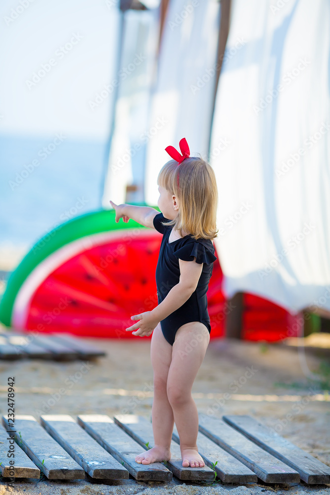 Obraz premium Summer lifestyle portrait of pretty girl swimming posing on the back on the inflatable watermelon in the ocean, wearing stylish bikini swim wear in black and hat. Relaxing and enjoying life.