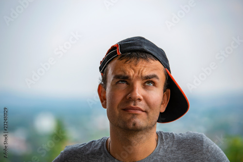 young man in a baseball cap ponders some idea by lifting up his eyes and squinting one eye.
