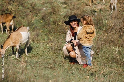 mother walks with little daughter near a herd of goats in autumn