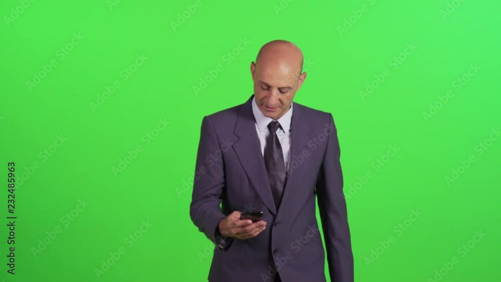 Businessman texting or using an app while walking towards camera, wearing a suit. Medium frontal shot over a green screen. Businessman texting or using an app while walking towards camera, wearing a suit. Medium frontal shot over a green screen.