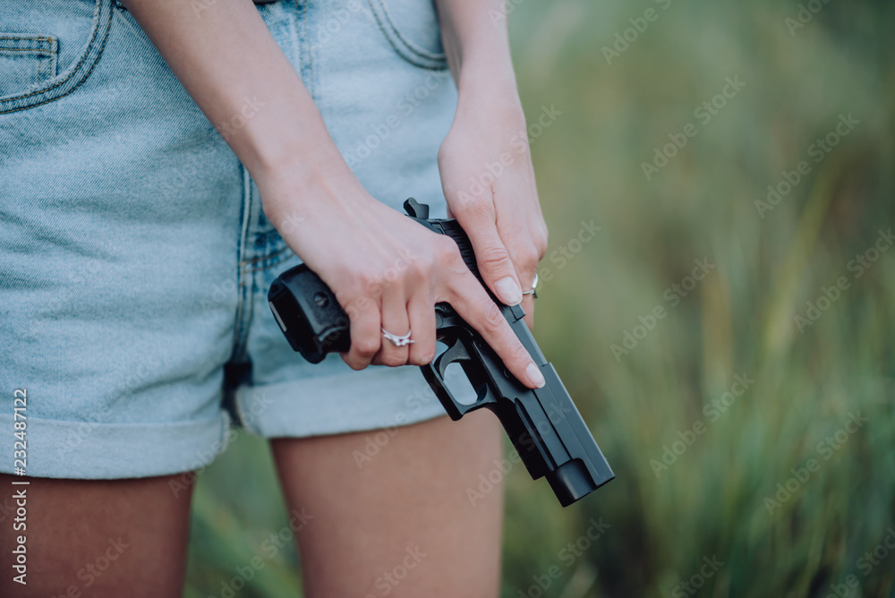 girl in denim shorts and with a gun in his hand posing in the field. Close up