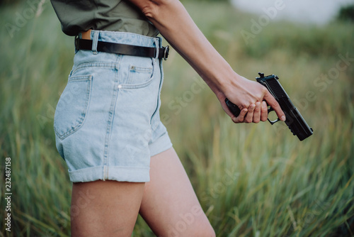 girl in denim shorts and with a gun in his hand posing in the field. Close up