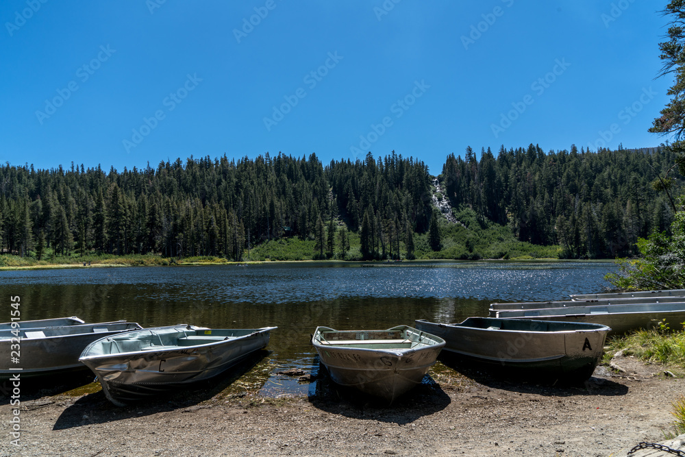 Aluminum boats parked on the shore of a lake with a waterfall in the middle of a background pine forest Aluminum boats parked on the shore of a lake with a waterfall in the middle of a background pine forest