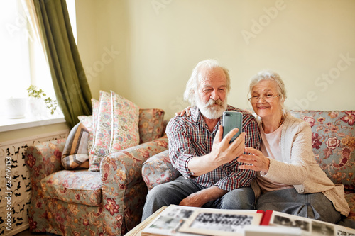 Happy senior retired grandmother and grandfather taking selfie with smartphone to send it to their grandchildren. Happy marriage concept