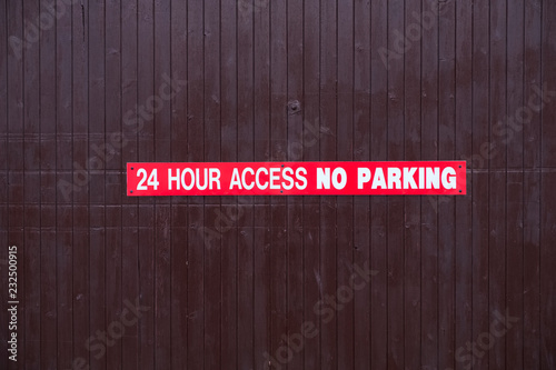 24 hour access no parking sign red and white on wooden access door